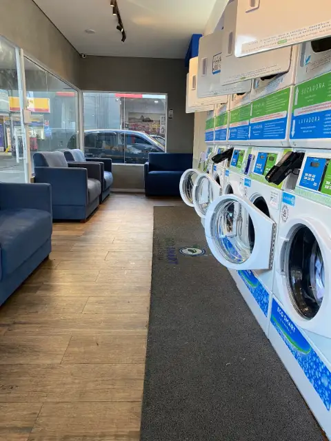 Salão da Eco Smart Lavanderia Cambuci com sofás, ar-condicionado e as lavadoras e secadoras self-service