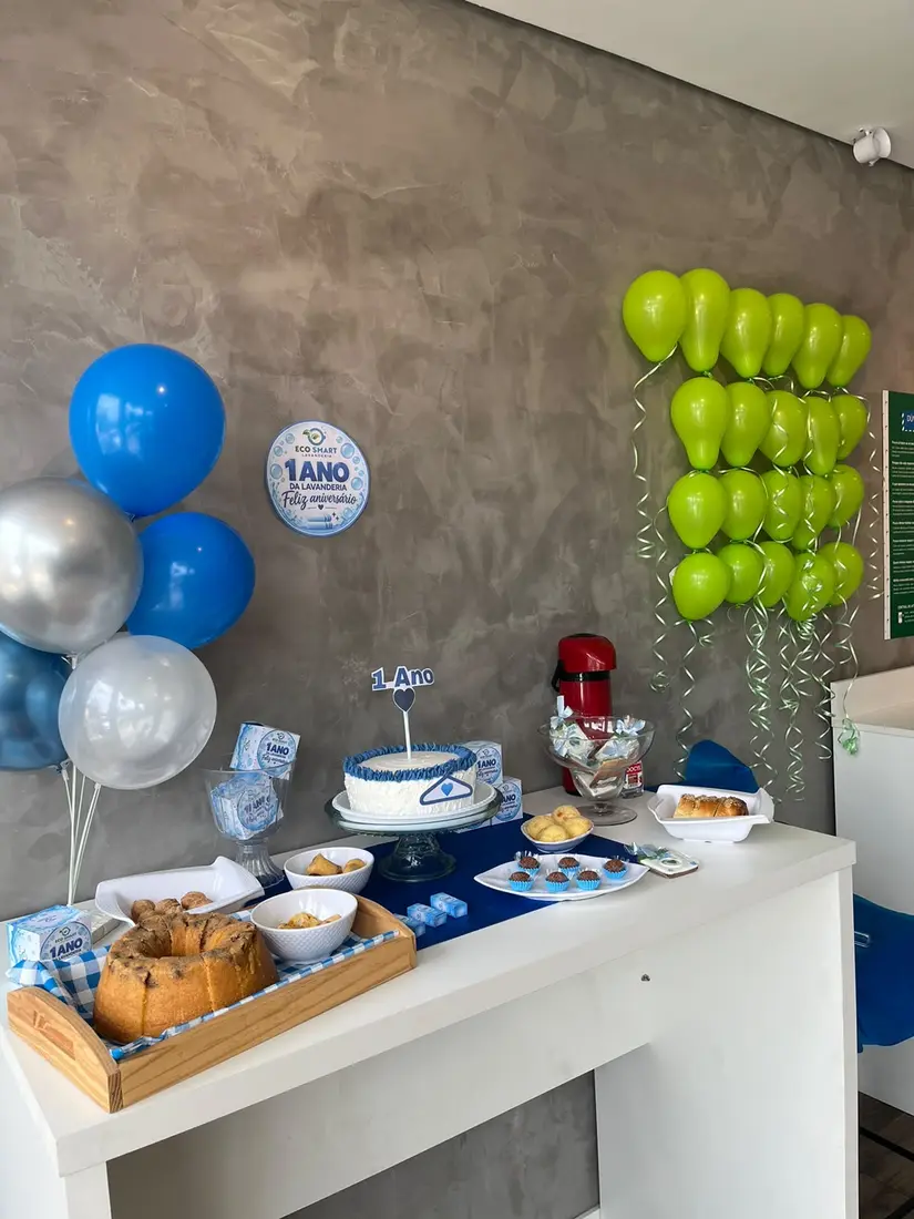 Mesa de aniversário de 1 ano da Eco Smart Lavanderia Valinhos, com bolo, salgados e balões nas cores da marca
